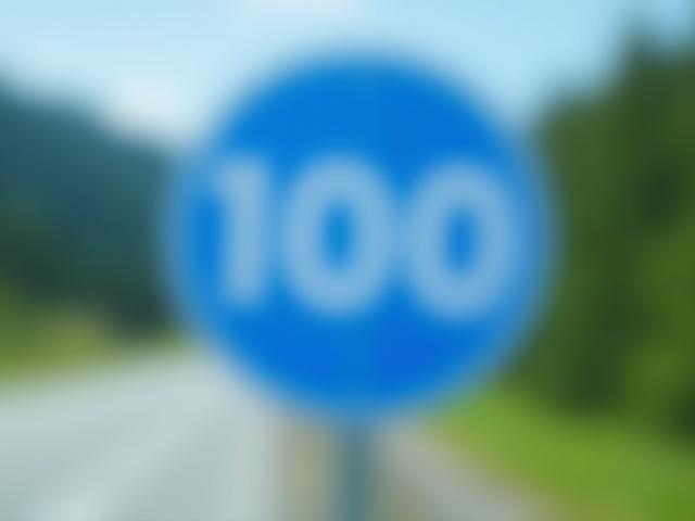Ein blaues Schild mit der weißen Zahl 100, das die Geschwindigkeitsbegrenzung auf einer österreichischen Straße anzeigt.